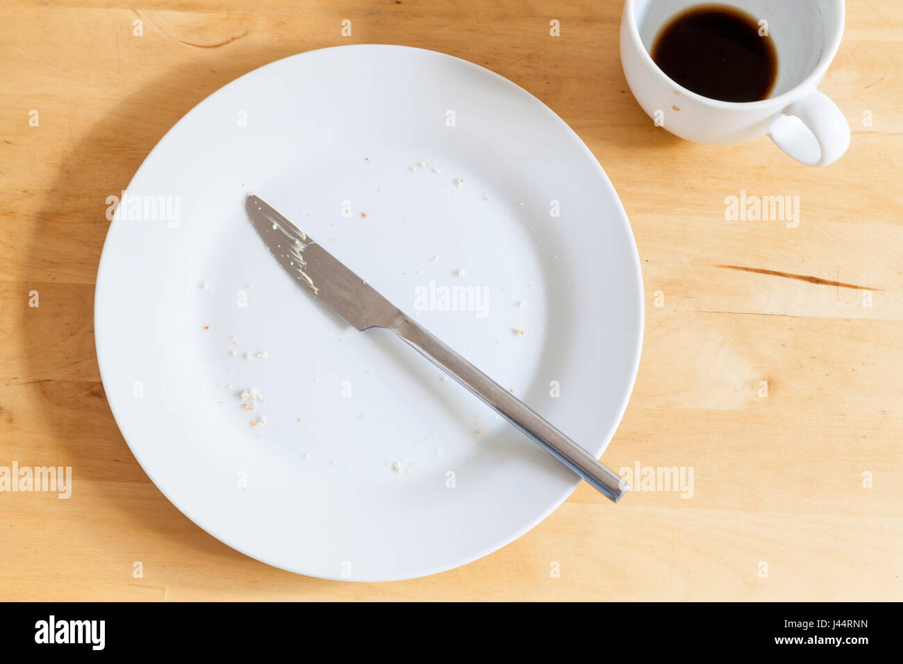 Fini de manger. Les restes ; une plaque avec des miettes, un couteau utilisé et la tasse de café vide après le petit-déjeuner ou snack en milieu de matinée Banque D'Images