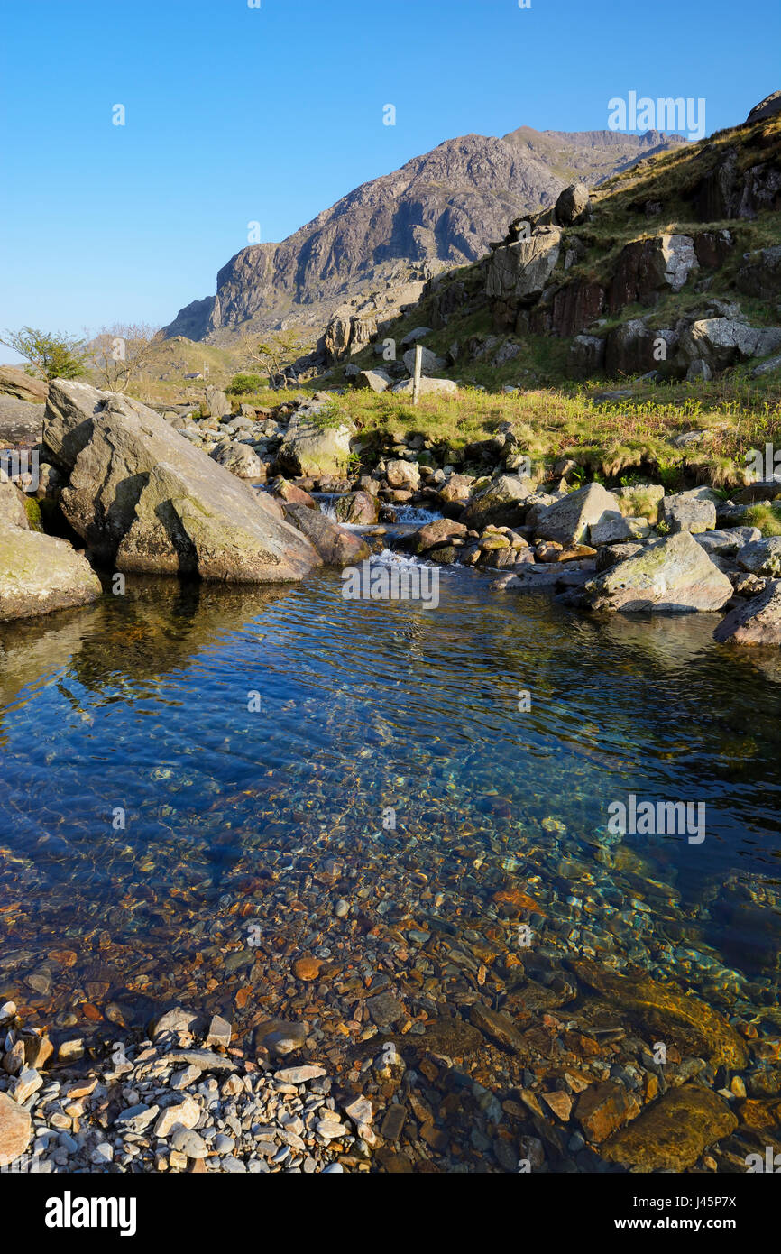 L'eau limpide de l'Afon Nant Peris dans le Llanberis Pass avec les falaises de redoutables Dinas Mot dans l'arrière-plan avec lit-bébé Coch (crête rouge), un kn Banque D'Images