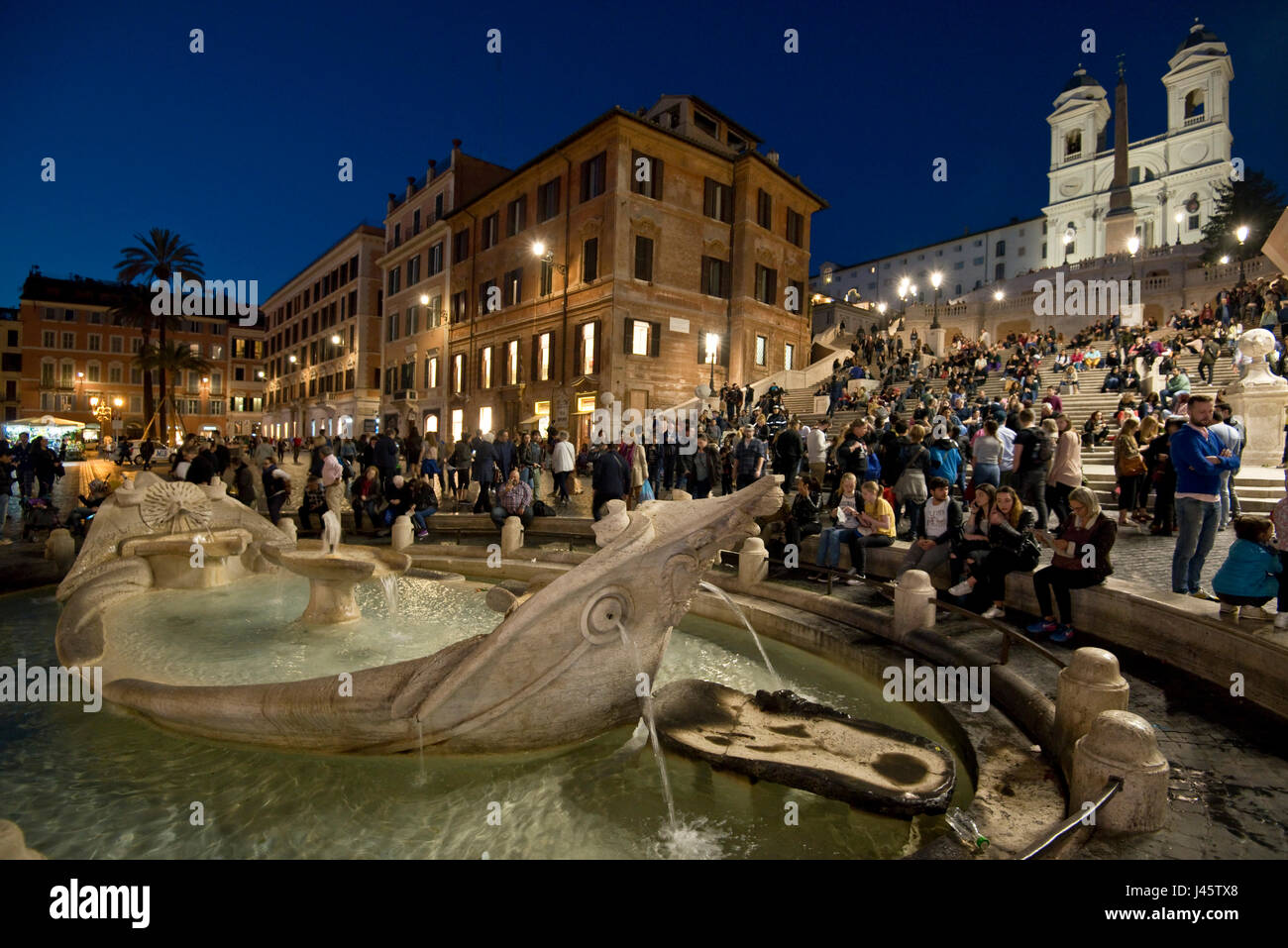 Place d'Espagne à Rome avec les touristes et les visiteurs de soirée, la nuit avec le fond de l'église Trinità dei Monti et fontaine de l'affreux voile avant-plan. Banque D'Images