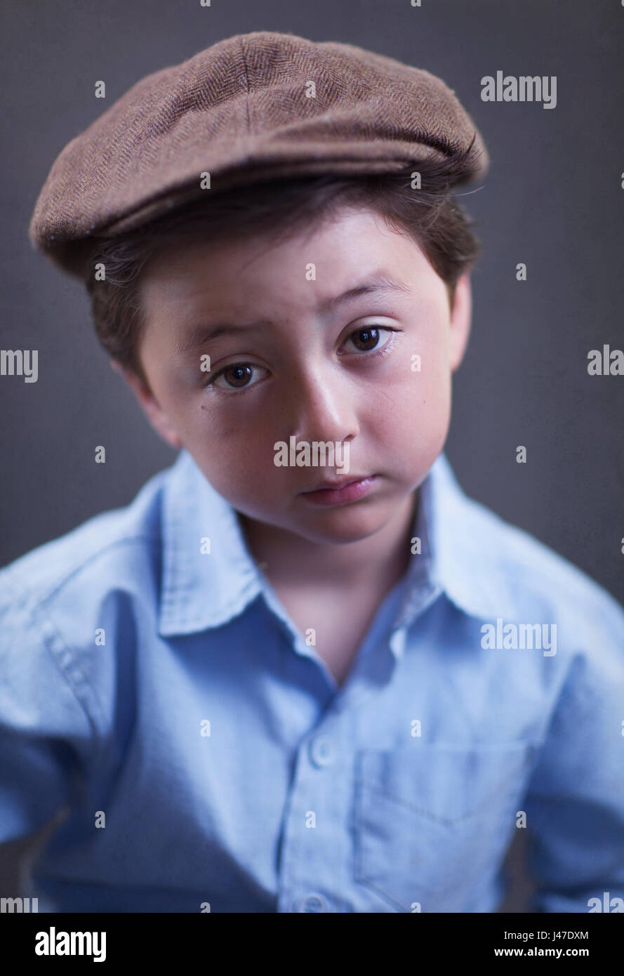 Mignon et sérieux à la recherche d'Asie multi-raciale portrait petit garçon vêtu d'un polo bleu et un chapeau gavroche tweed marron Banque D'Images