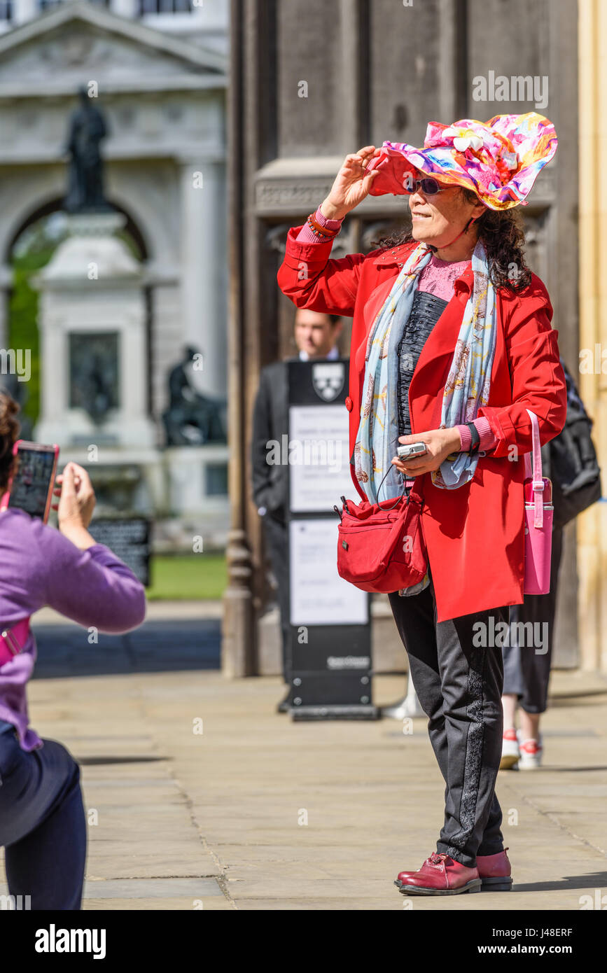 Une femme, de touristes chinois avec un manteau rouge et sac et un chapeau fleuri, pose pour une photo en face de l'entrée principale de King's College de l'uni Banque D'Images