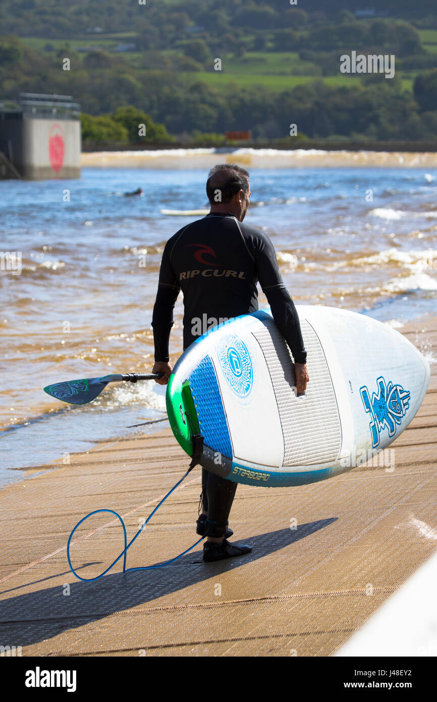 Marcher avec un surfeur surf board à la piscine à vagues artificielles dans la vallée de Conwy connu comme Snowdonia Surf Banque D'Images