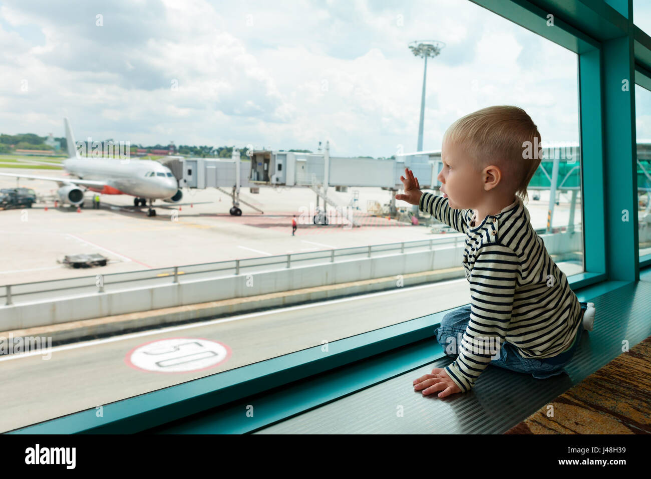 Little baby boy waiting l'embarquement à l'aéroport en vol et l'hôtel de transit à travers la fenêtre de l'avion à près de d'embarquement. Vie de famille actifs Banque D'Images