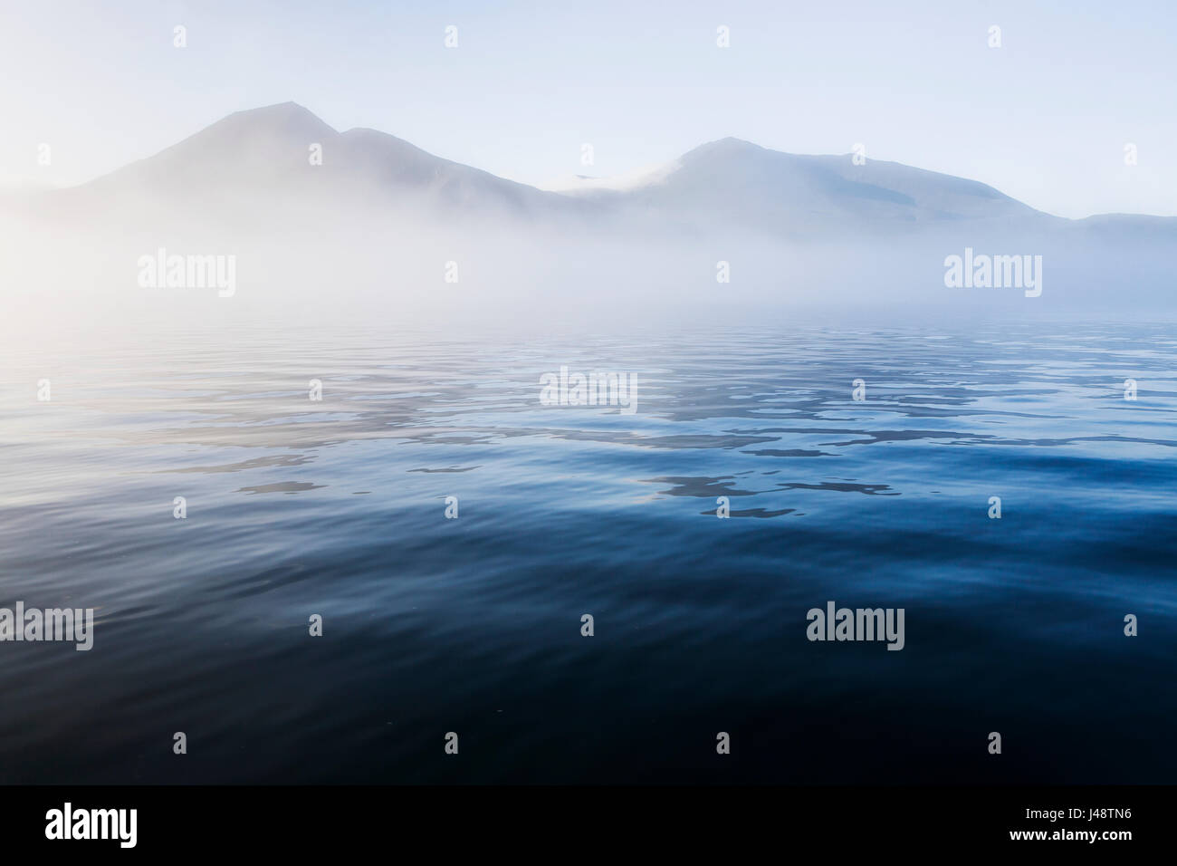 L'océan bleu entourant les îles Aléoutiennes mène dans un banc de brouillard dissimulant partiellement la vue de montagnes et Volcans Banque D'Images