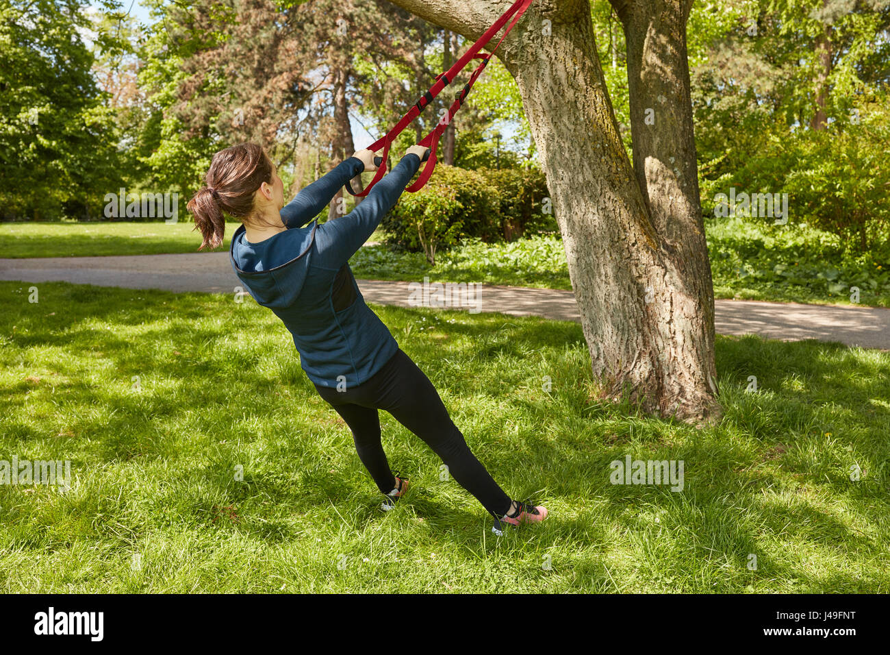 Jeune femme faisant la formation de l'élingue au parc avec arbres Banque D'Images