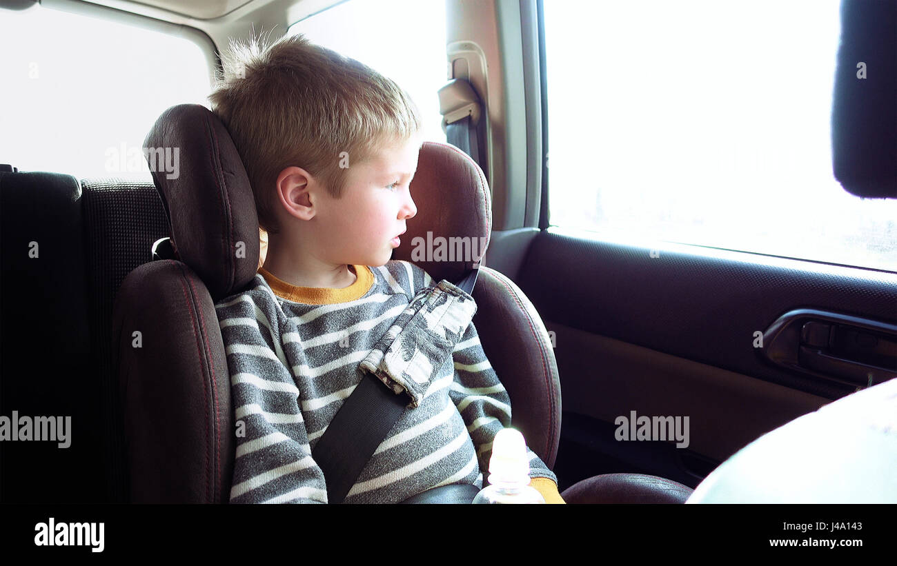 Cute boy dans un siège d'auto pour enfant regarde par la fenêtre Banque D'Images