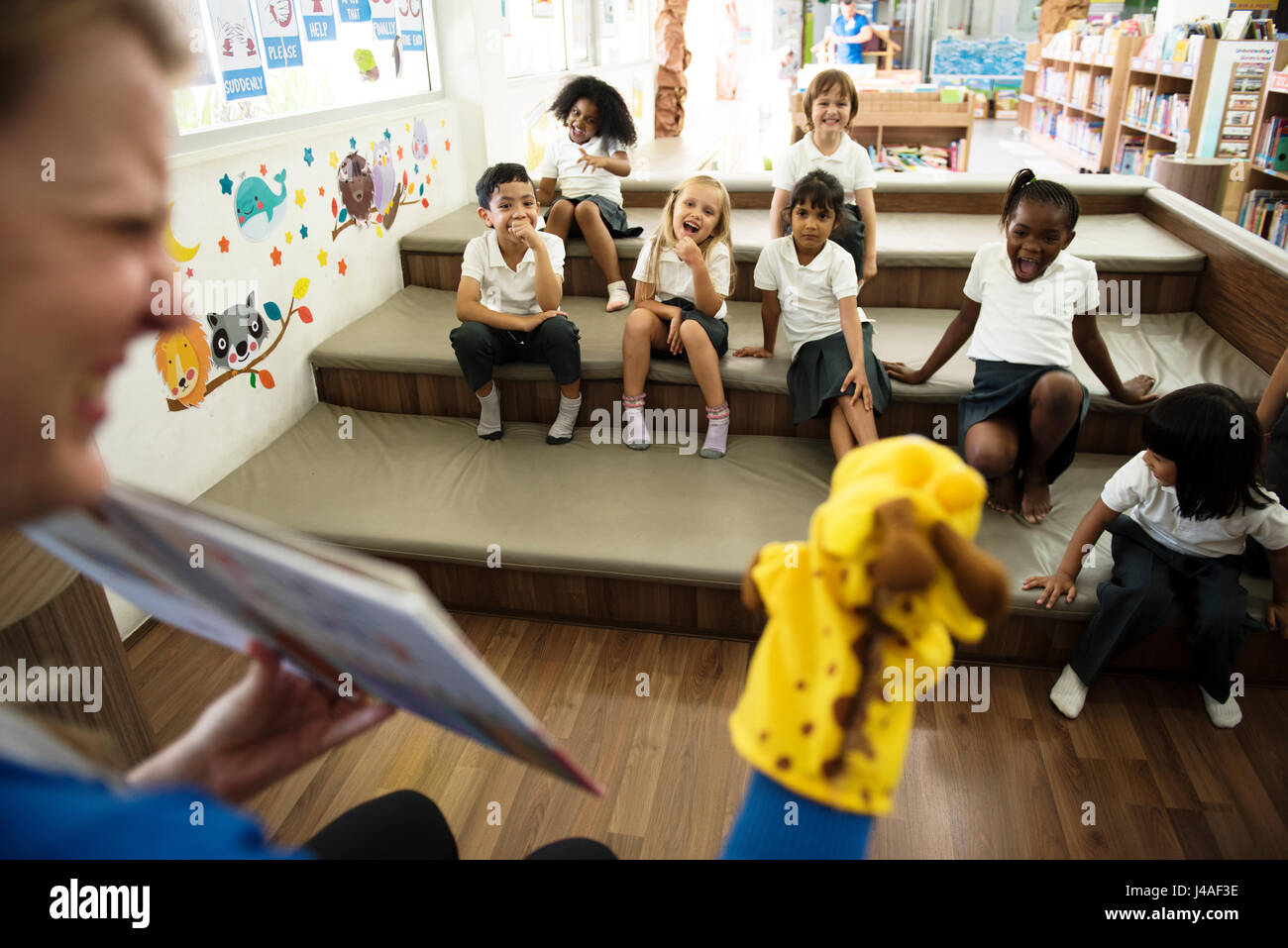 Les élèves de maternelle assis sur le plancher à l'écoute de contes Banque D'Images