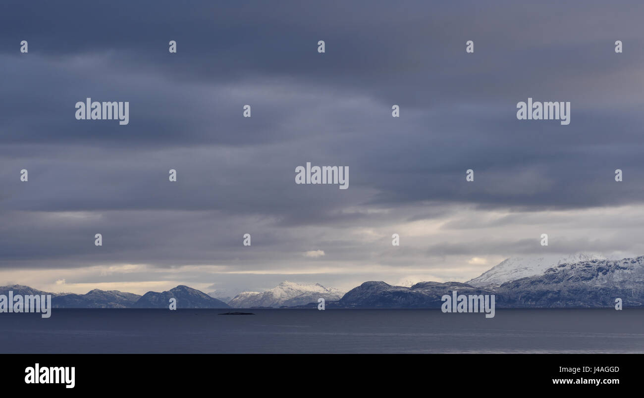 Un tableau sombre, nuageux, gris ciel d'hiver sur la mer et les îles de neige près de Harstad. Harstad, Troms, Norvège. Banque D'Images