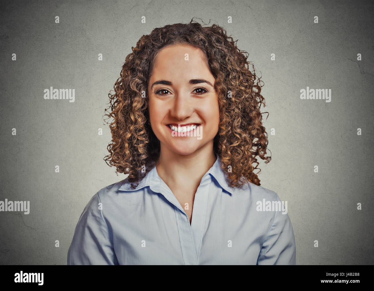 Closeup portrait portrait, belle jeune femme d'affaires avec les cheveux bouclés en bleu shirt smiling isolé sur fond de mur gris. Les droits positifs emoti Banque D'Images