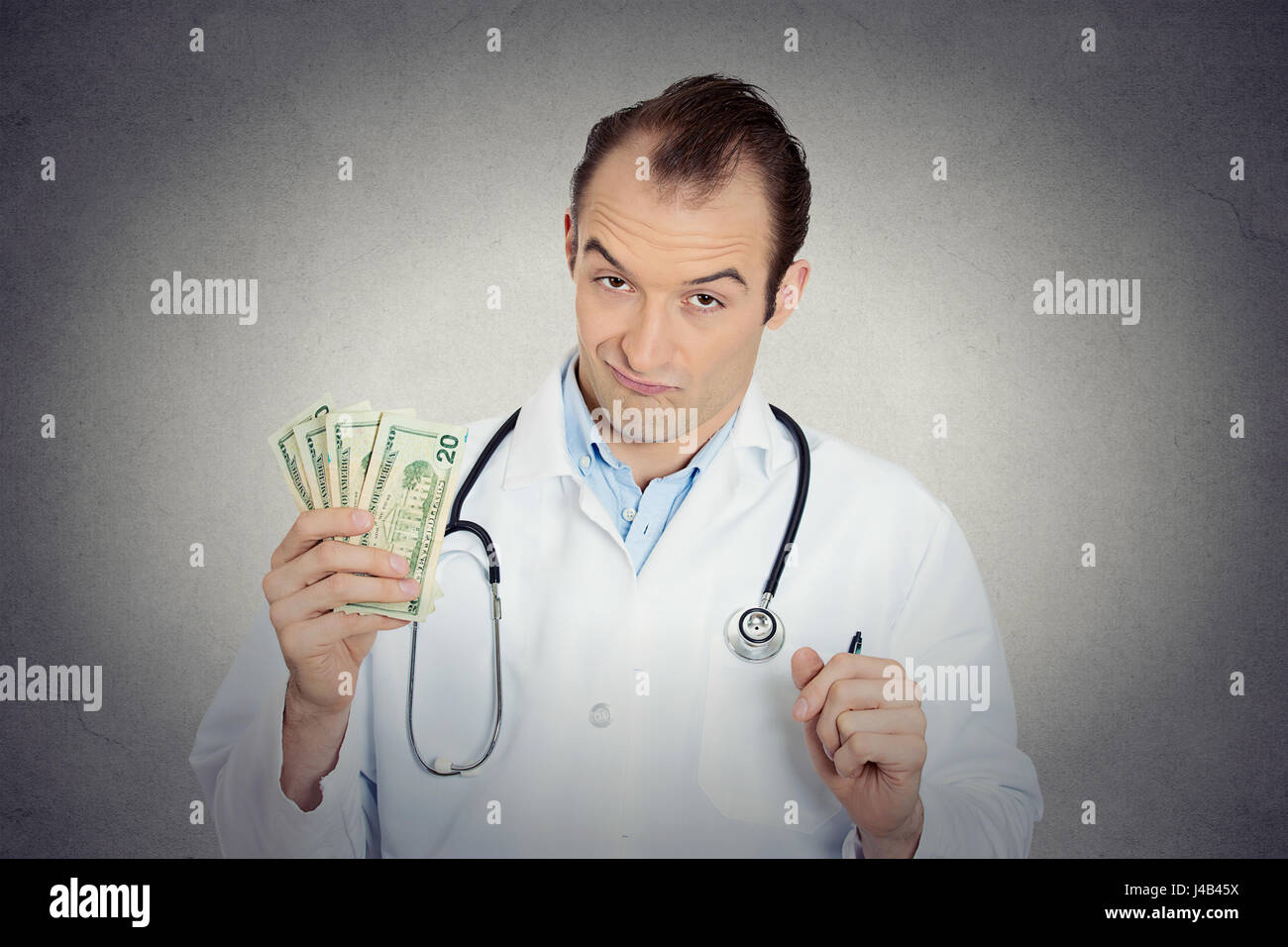 Closeup portrait avide avare grincheux professionnel de la santé, male doctor holding, protéger son argent dollars dans la main de mur gris isolé backgrou Banque D'Images