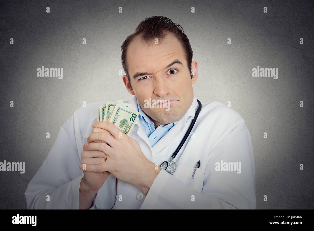 Closeup portrait avide avare grincheux professionnel de la santé, male doctor holding, protéger son argent dollars dans la main de mur gris isolé backgrou Banque D'Images