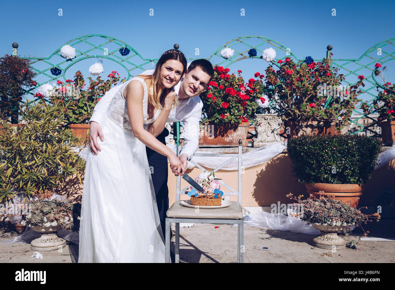 Salon de la mariée et le marié sont beau découpage d'un gâteau de mariage. Couple sur la terrasse avec la ville de Rome dans l'arrière-plan. Beau modèle girl in white Banque D'Images