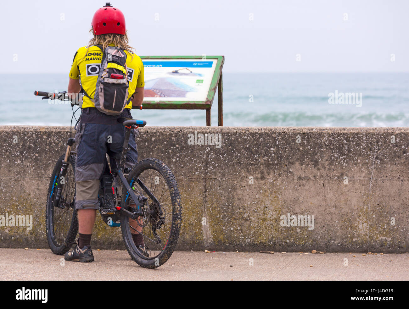 Un homme à vélo, cycliste, s'est arrêté sur la promenade en signe d'information à la promenade de l'esplanade de la plage de Weymouth, Weymouth, Dorset UK en mai Banque D'Images