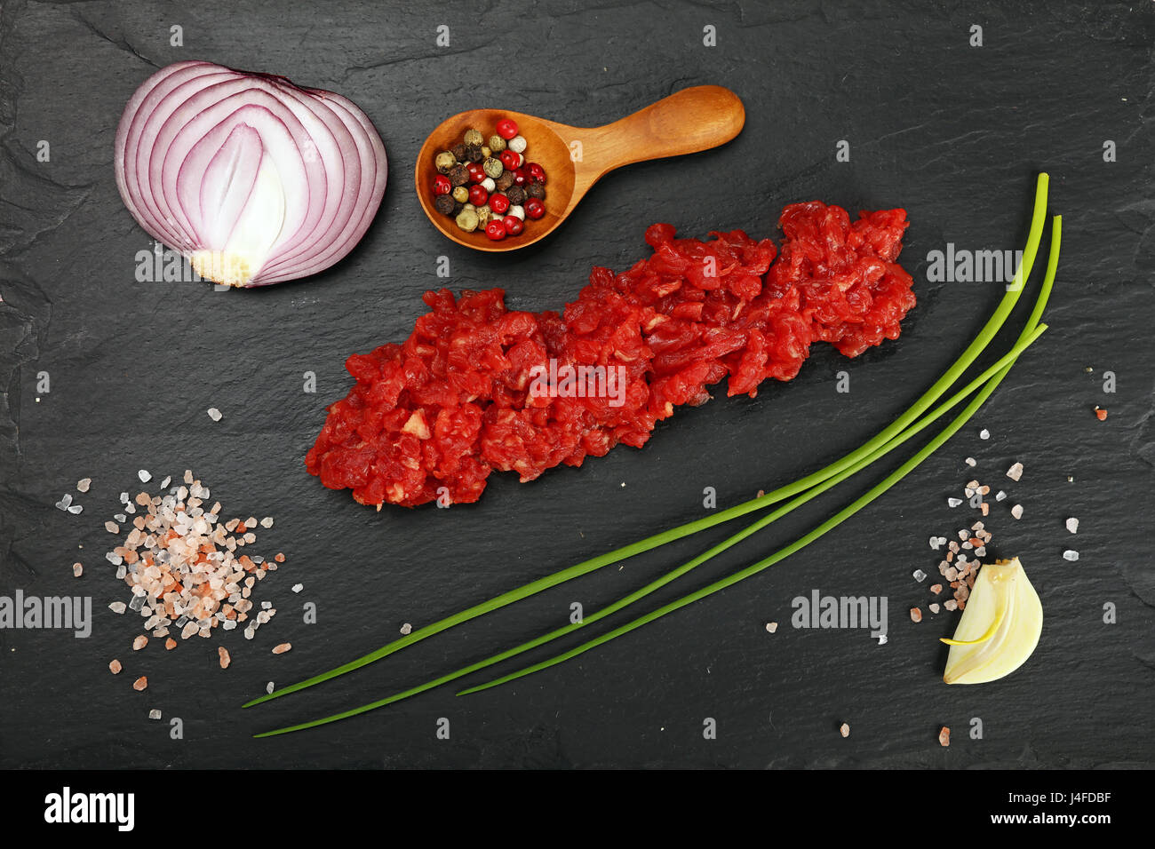 La viande hachée crue escalope de viande rouge, d'épices, poivre, l'échalote, l'ail les oignons de printemps et le sel sur l'ardoise noire, Close up, augmentation de la vue d'en haut, Banque D'Images