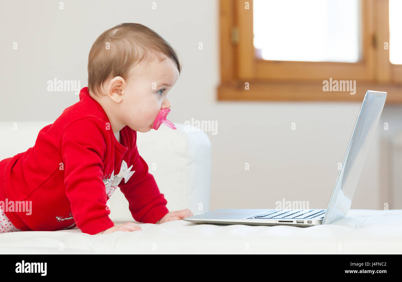 8 mois bébé fille à l'aide d'un ordinateur portable sur le canapé à la maison. Banque D'Images