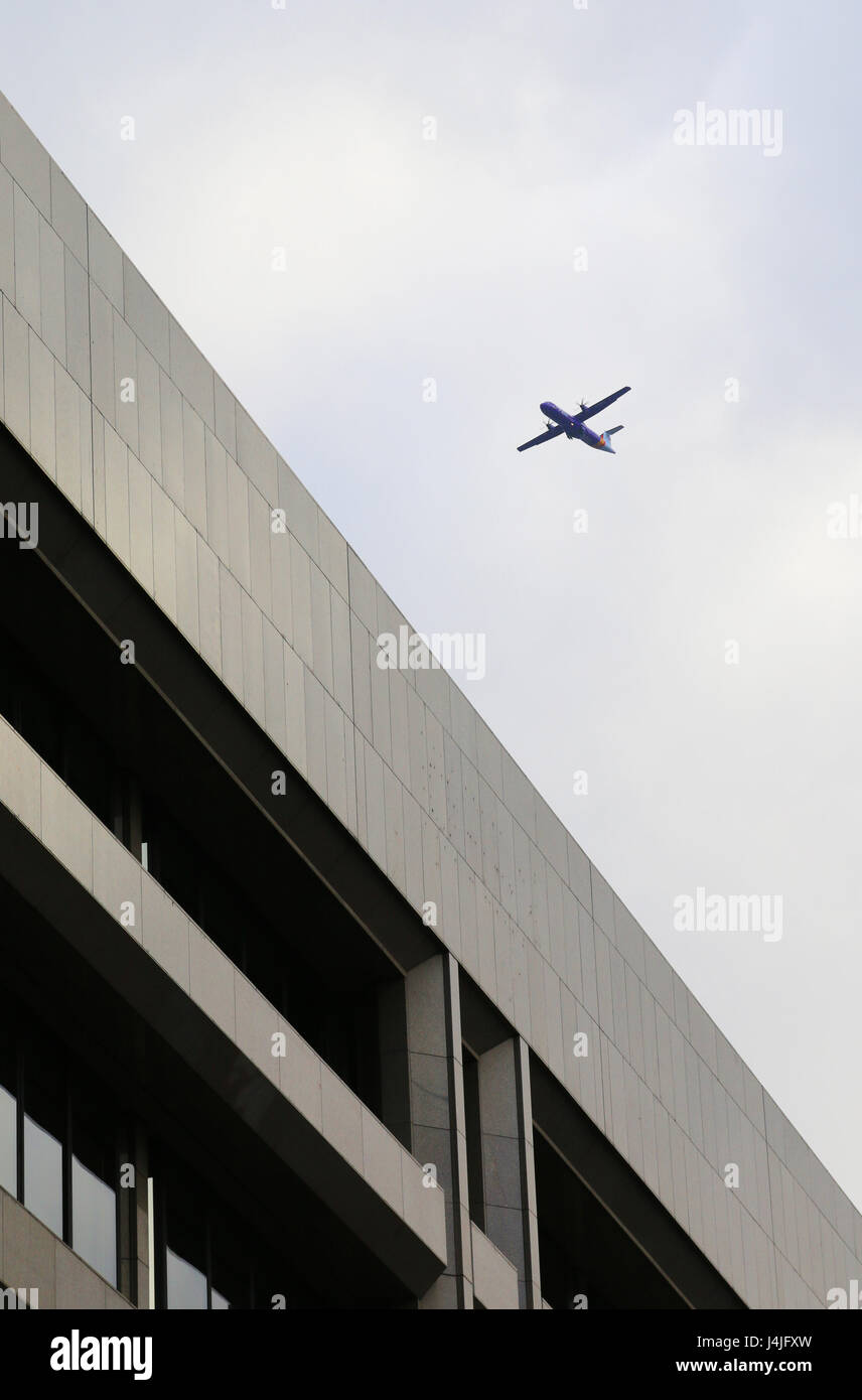 Avion au décollage derrière office building against cloudy sky Banque D'Images