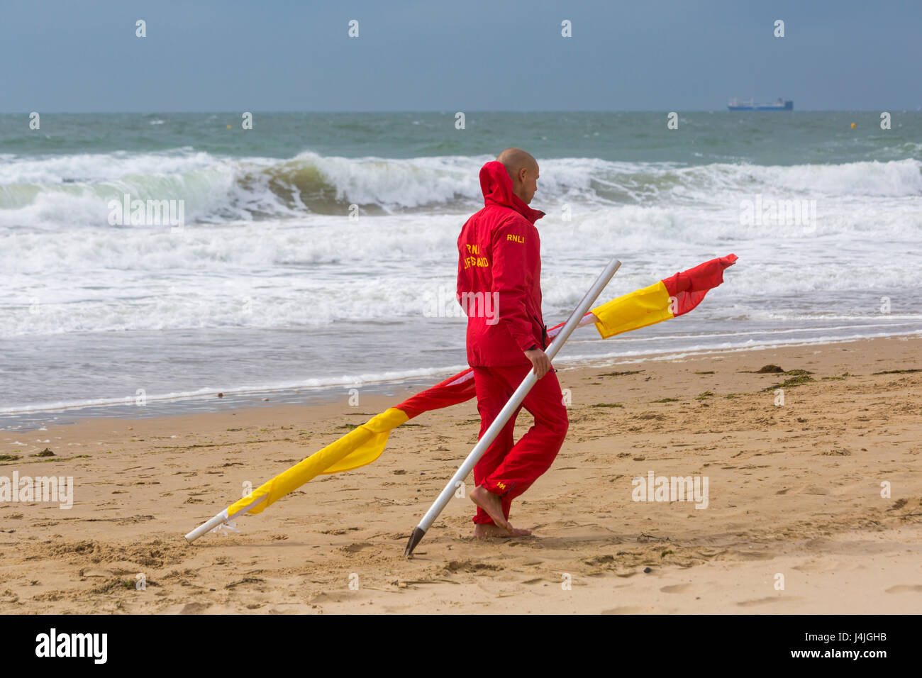 Sauveteur RNLI portant les drapeaux rouge et jaune indiquant zone sécuritaire de nager au bord de la mer, sur la plage de Bournemouth, Dorset en Avril Banque D'Images