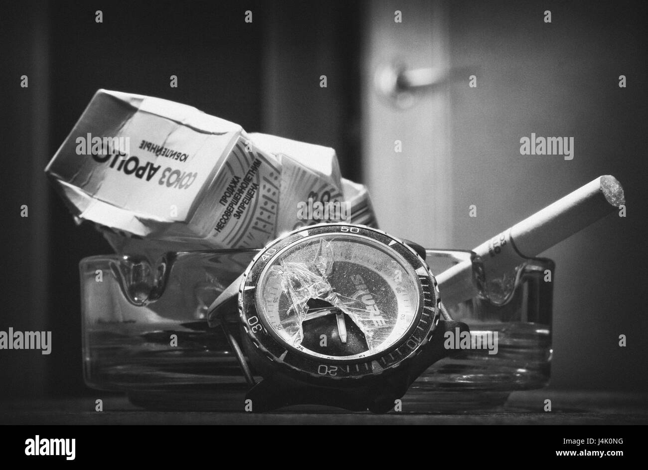 Un réveil cassé sur l'arrière-plan d'un paquet de cigarettes froissé. La vie toujours en noir et blanc. Banque D'Images
