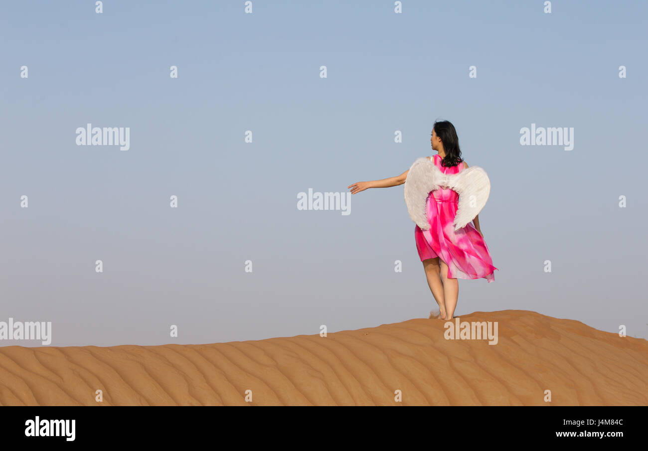 Jeune femme avec des ailes d'angle dans un désert Banque D'Images