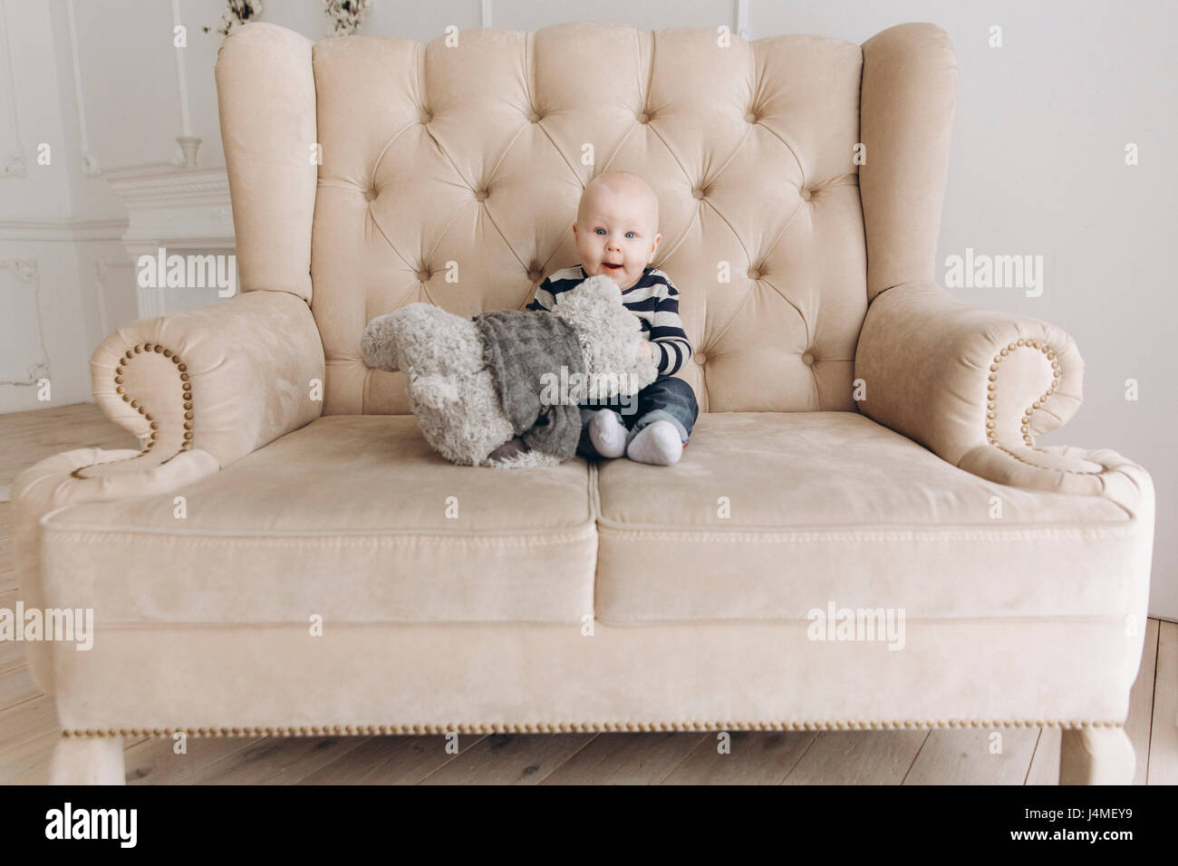 Caucasian baby boy sitting on love seat jouer avec teddy bear Banque D'Images