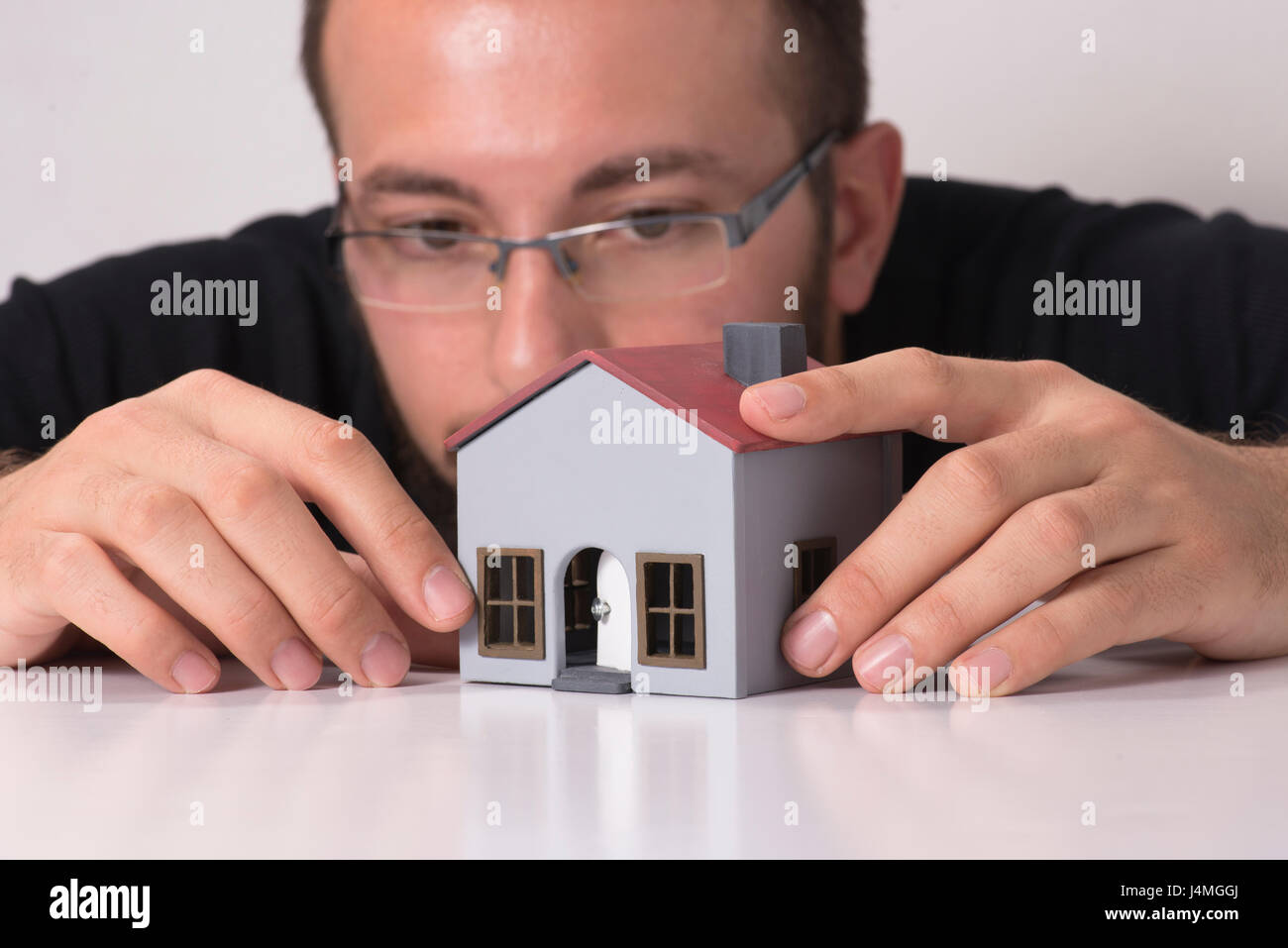 L'homme de prendre un regard étroit à la maison modèle sur un fond blanc. Banque D'Images