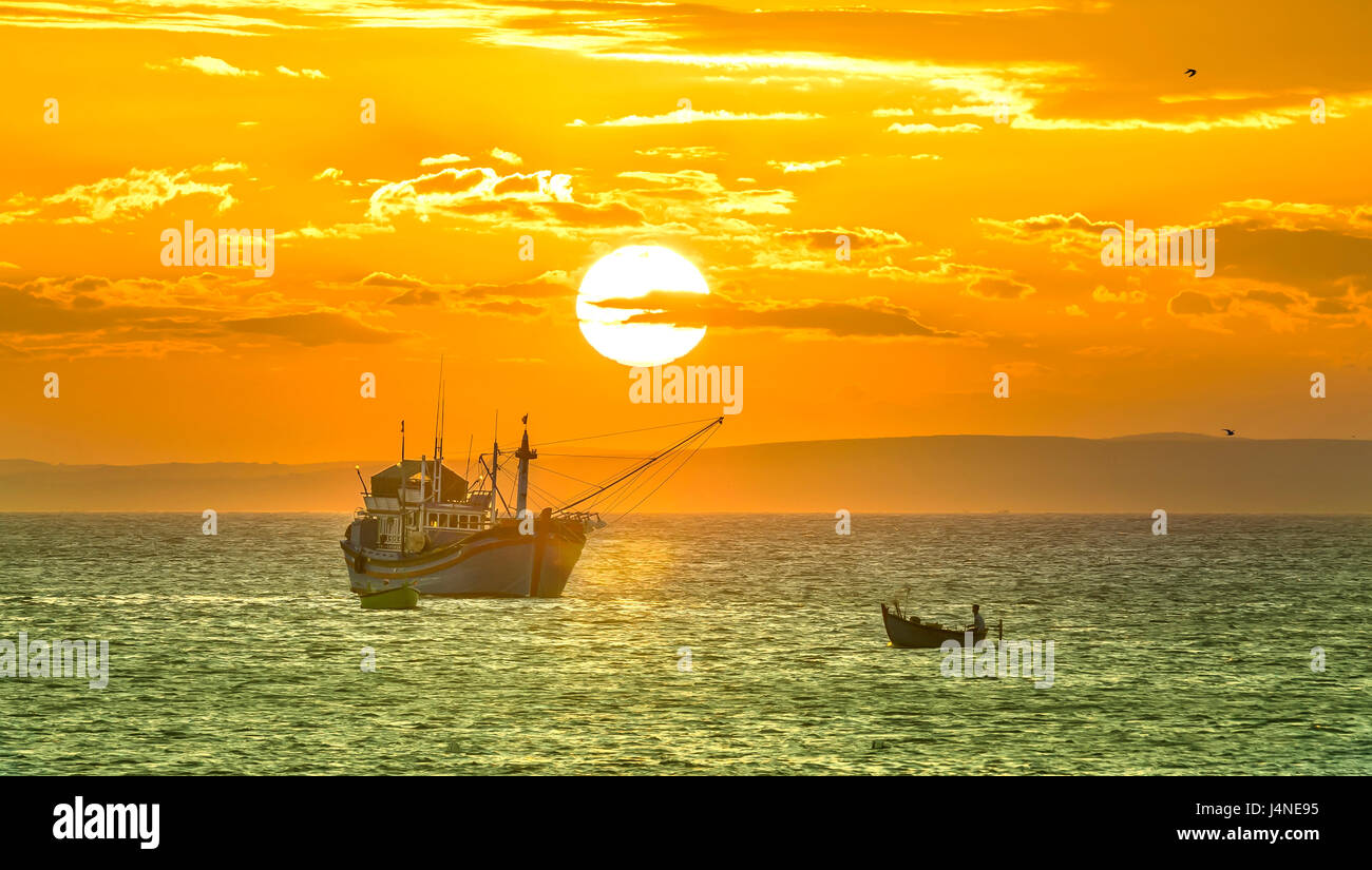 Le coucher et le bateau sur la mer que le soleil lentement sur l'horizon crée une belle lumière dorée sur la baie Banque D'Images