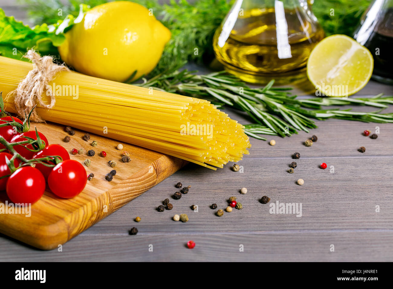 Spaghetti, tomates cerise, huile d'olive, d'herbes et épices sur le vieux fond de bois gris. Définir pour des aliments sains. Ingrédients pour la salade Banque D'Images