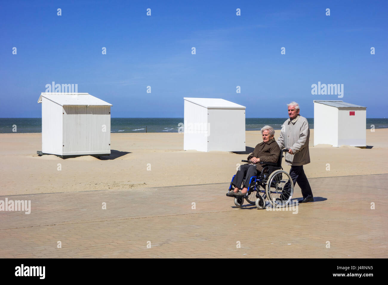 Mari à la retraite prendre femme âgées handicapées en fauteuil roulant pour une promenade sur la promenade le long de la côte par une froide journée ensoleillée au printemps Banque D'Images