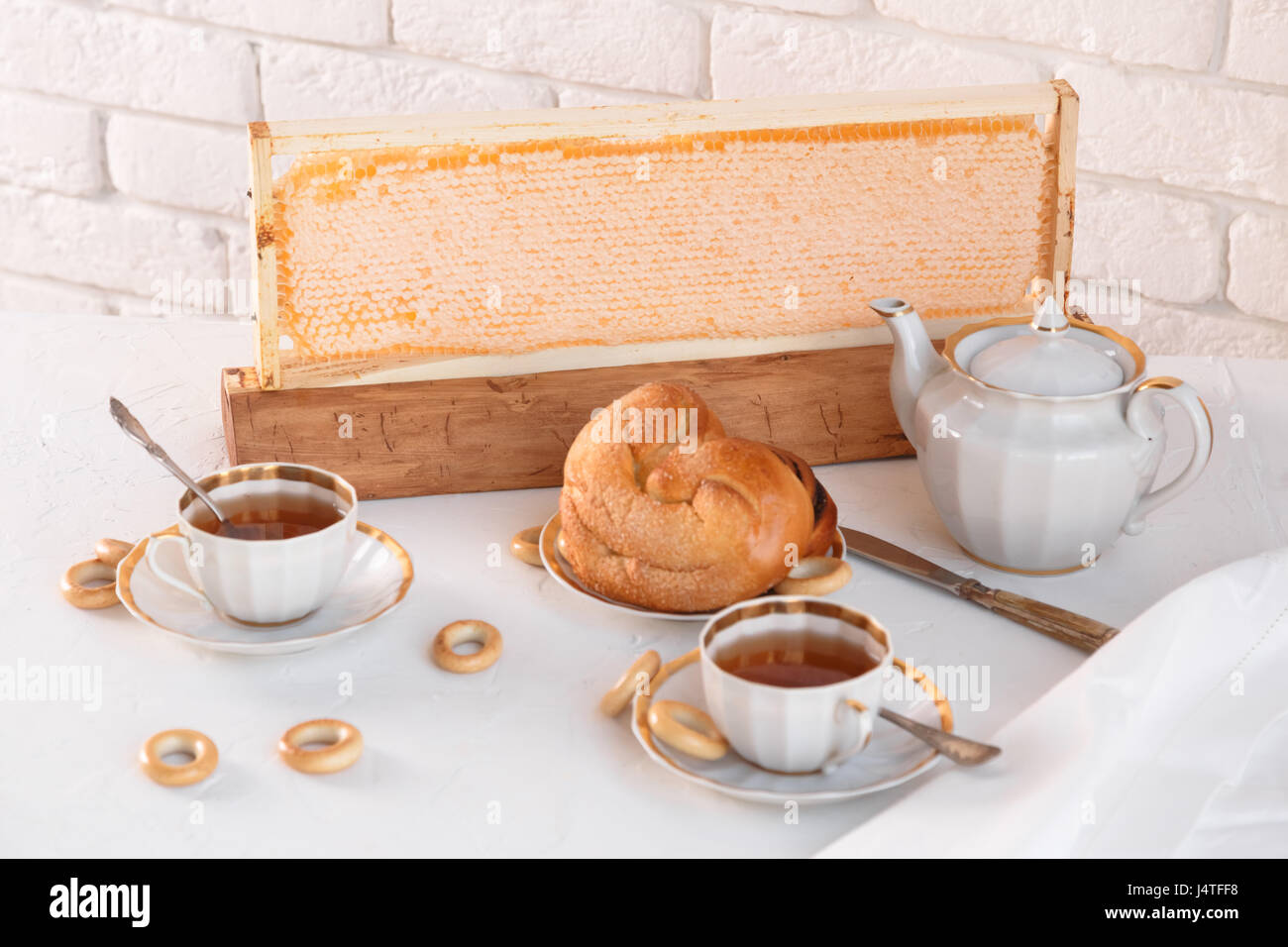 Tasses de Thé et une théière avec le miel, les brioches sur fond brique blanche Banque D'Images