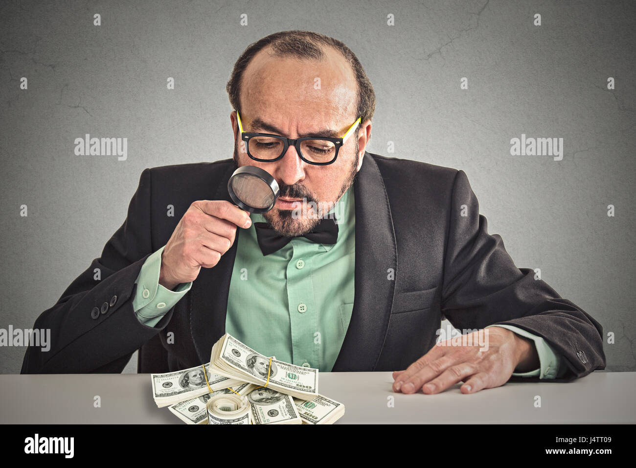 Penny Pincher. L'homme d'affaires à la recherche à travers une loupe sur pile de billets de un dollar sur la table bureau gris isolé arrière-plan. Économie Banque D'Images