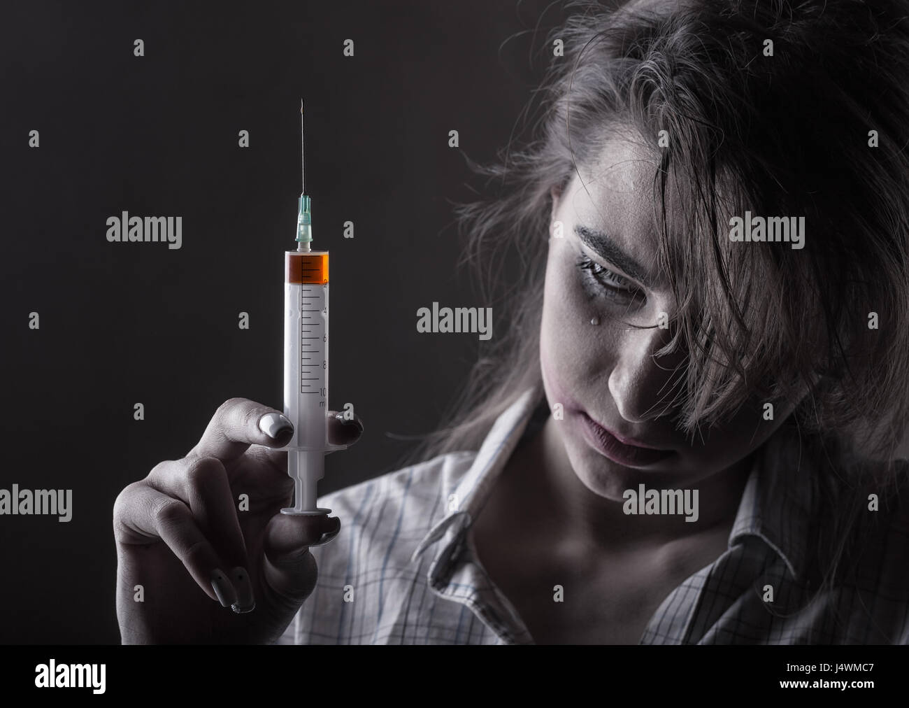 Jeune femme avec la toxicomanie sur fond sombre. L'accent sur seringue Banque D'Images