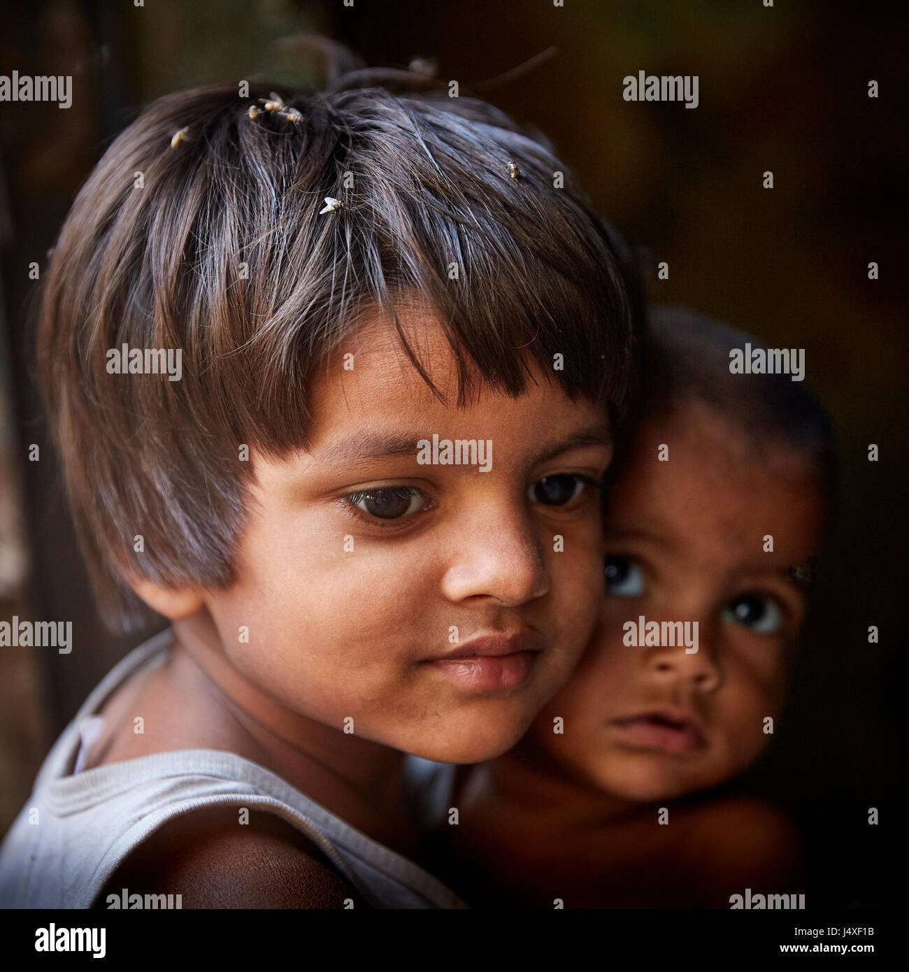 Fille indienne à New Delhi slum head and shoulders portrait à l'écart et en bas de l'appareil photo avec un frère dans l'arrière-plan foncé looking at camera Banque D'Images