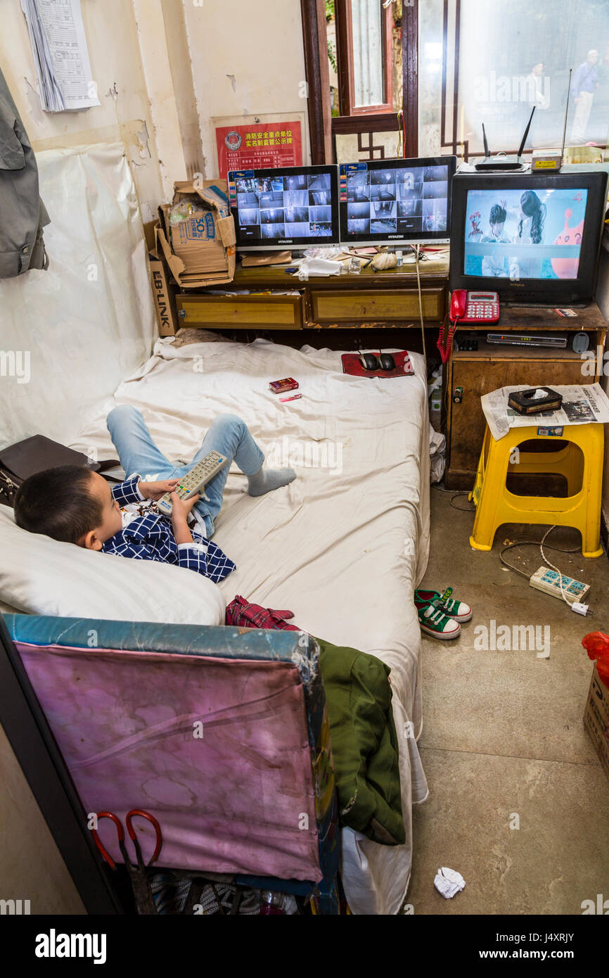 Zhenyuan, Guizhou, en Chine. Jeune garçon regardant la télévision dans sa chambre, à l'aide de la télécommande. Banque D'Images