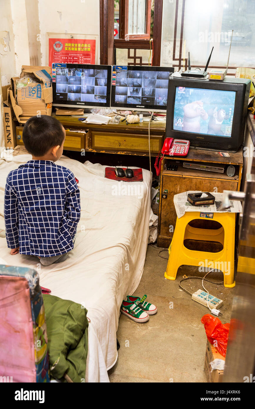 Zhenyuan, Guizhou, en Chine. Jeune garçon regardant la télévision dans sa chambre. Banque D'Images