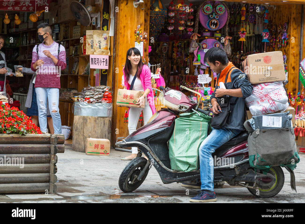 Zhenyuan, Guizhou, en Chine. L'homme en moto faire une livraison. Remarque client avec masque de protection des voies respiratoires. Banque D'Images