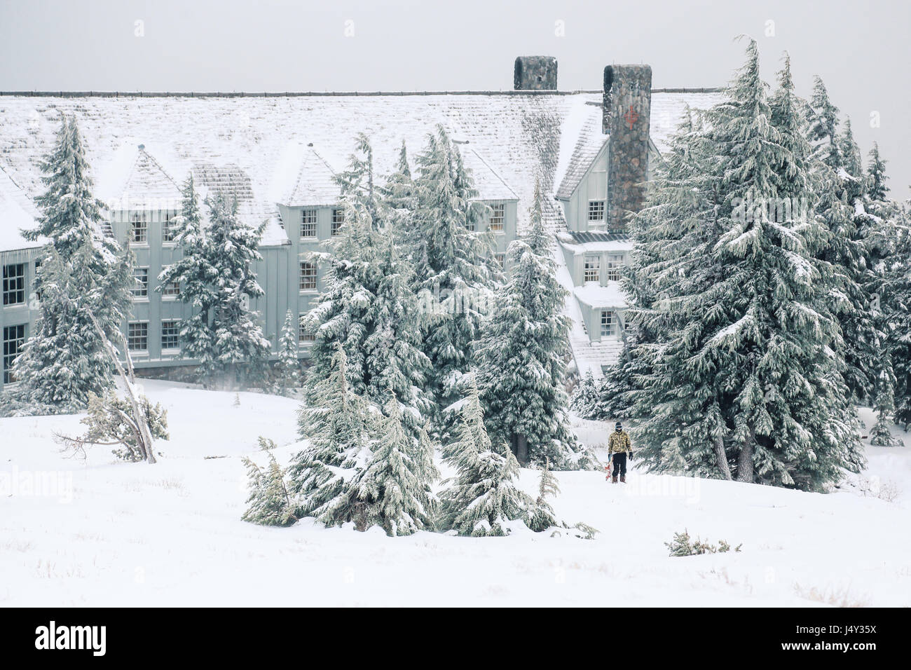 Un homme avec son snowboard se tient juste en face de Timberline Lodge, sur le mont Hood dans l'Oregon. Banque D'Images