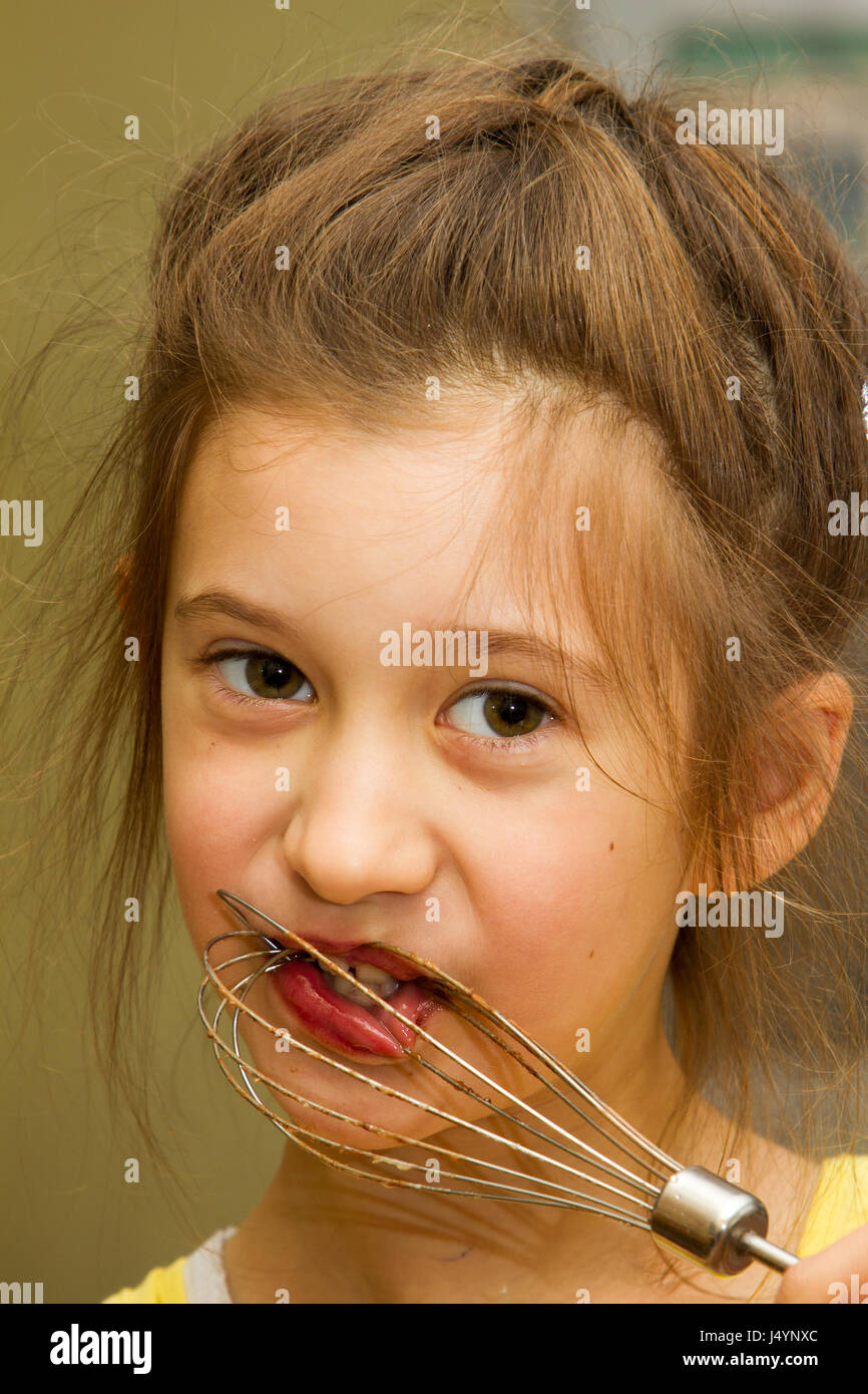 Petite fille léchant le chocolat de batteur mélangeur après mélange de la pâte à gâteau d'anniversaire. La parentalité permissive, l'apprentissage par l'expérience, l'inclusion de l'enfant, une cuisine maison concept. Banque D'Images