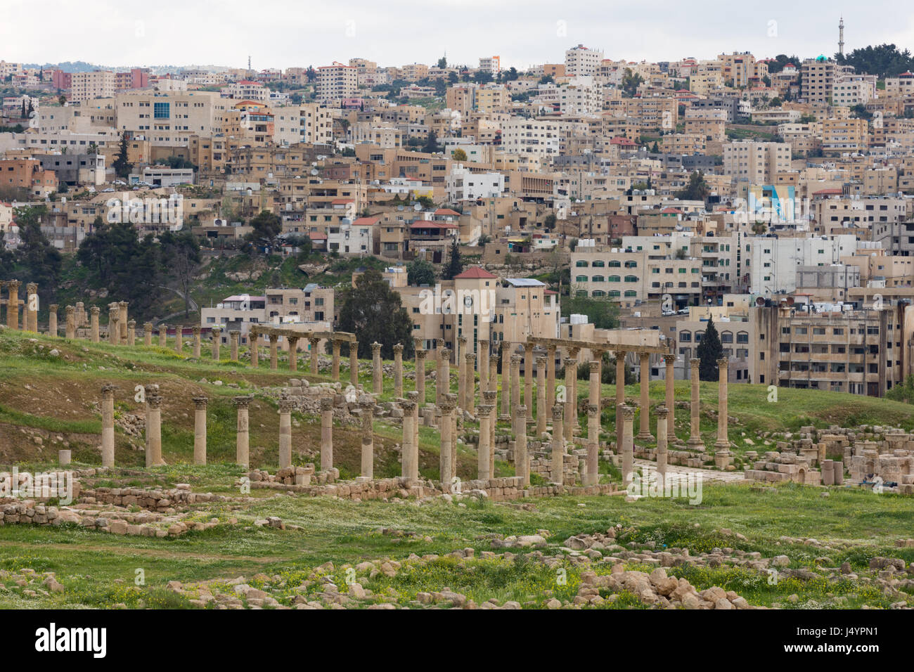 Colonnes et chapiteaux en pierre de la rue à colonnade dans l'ancienne cité romaine de Jerash, ville de commerce Jordanie. La ville moderne s'est vu dans l'arrière-plan. Banque D'Images