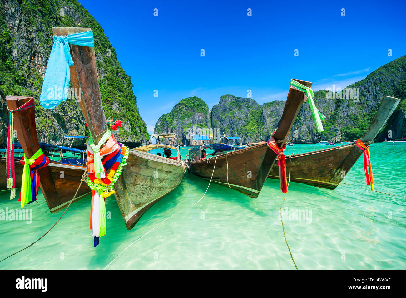 Bateaux longtail en bois traditionnel thaï avec des écharpes colorées dans les eaux turquoise de la baie de Maya d'Andaman, dans le sud de la Thaïlande Banque D'Images