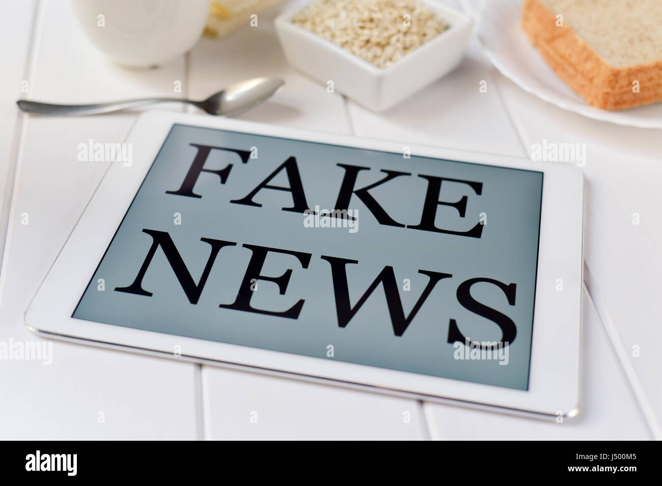 Libre d'un ordinateur tablette avec le texte de fausses nouvelles dans l'écran sur un tableau blanc pour le petit-déjeuner ensemble, avec un peu de céréales, une tasse de café et quelques chrit Banque D'Images