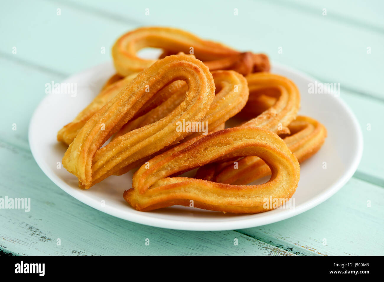 Libre de quelques churros typiques de l'Espagne sur une plaque en céramique blanc, placé sur une table rustique en bois vert pâle Banque D'Images