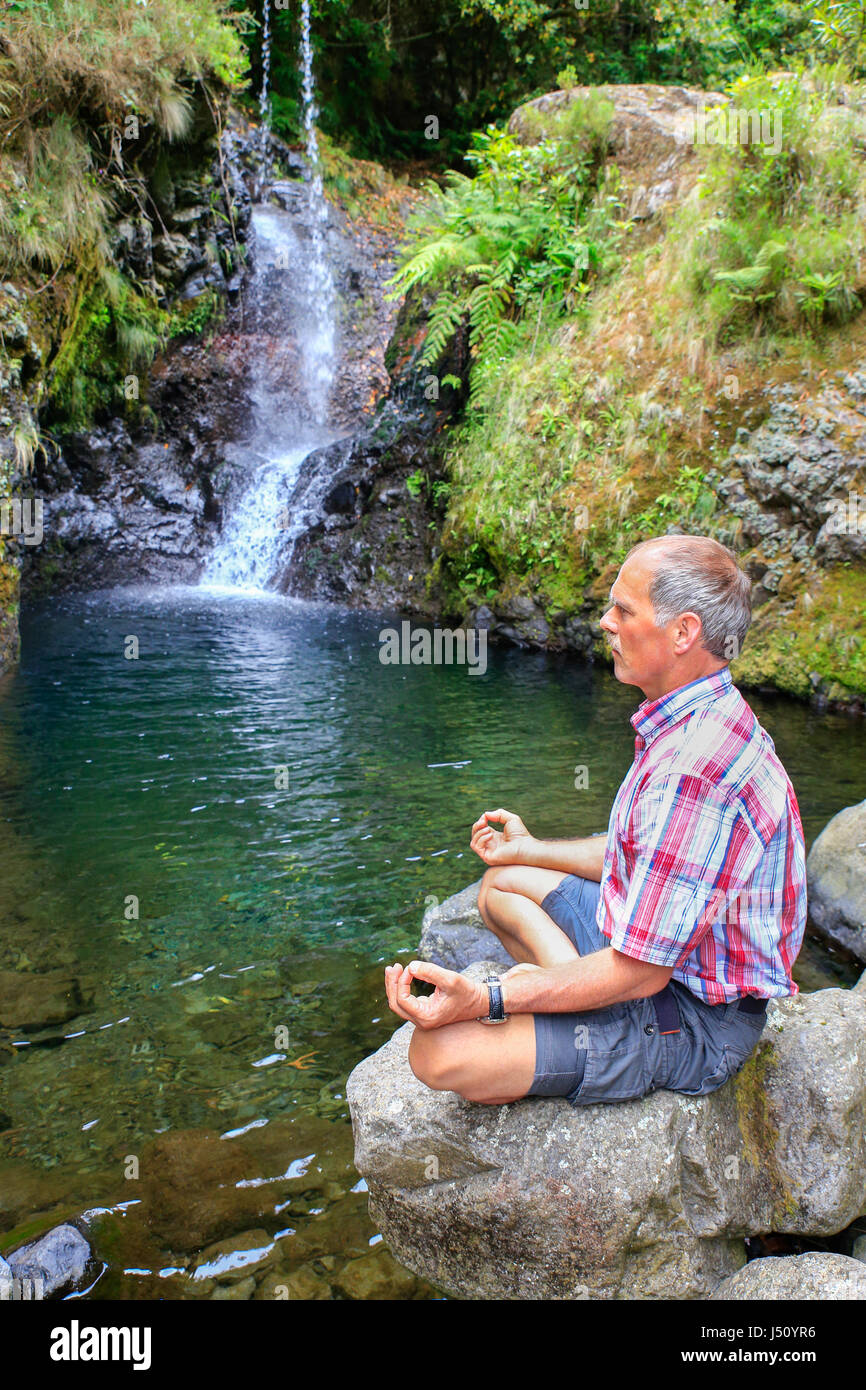 Dutch man sitting on rock méditer près de waterfall in Portugal Banque D'Images