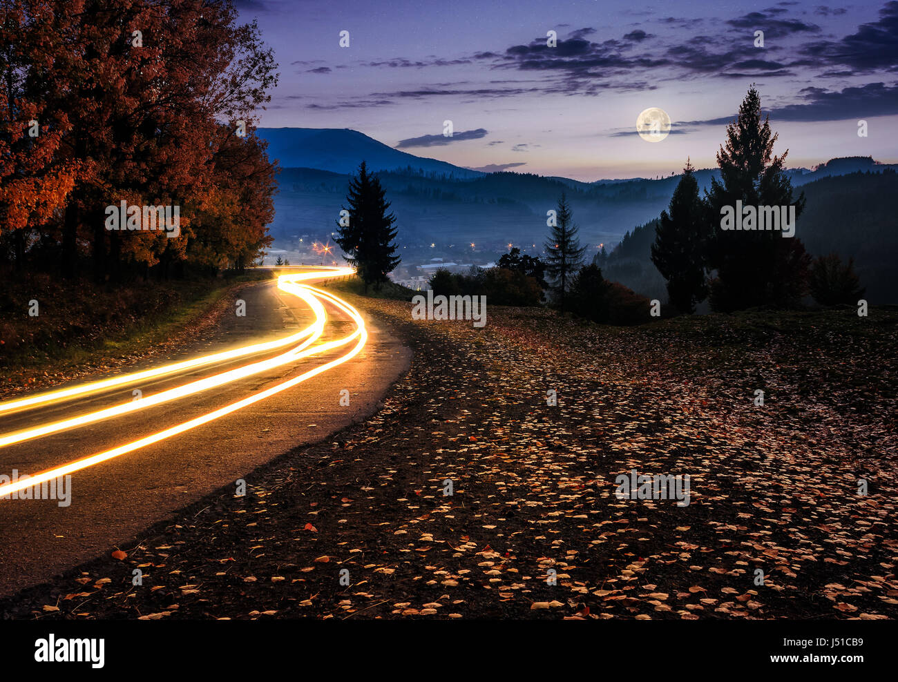 Route de campagne avec voiture. Belle automne paysage de montagne dans la nuit dans la lumière de la pleine lune Banque D'Images Route de campagne avec voiture. Belle automne paysage de montagne dans la nuit dans la lumière de la pleine lune Banque D'Images