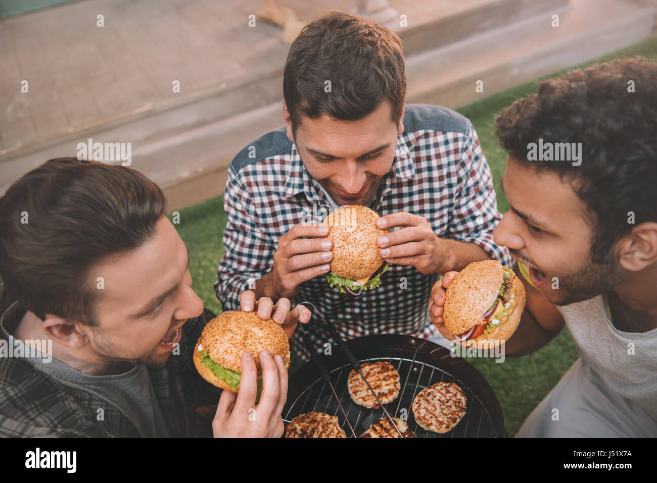 Portrait de trois jeunes hommes manger des hamburgers grill ci-dessus Banque D'Images