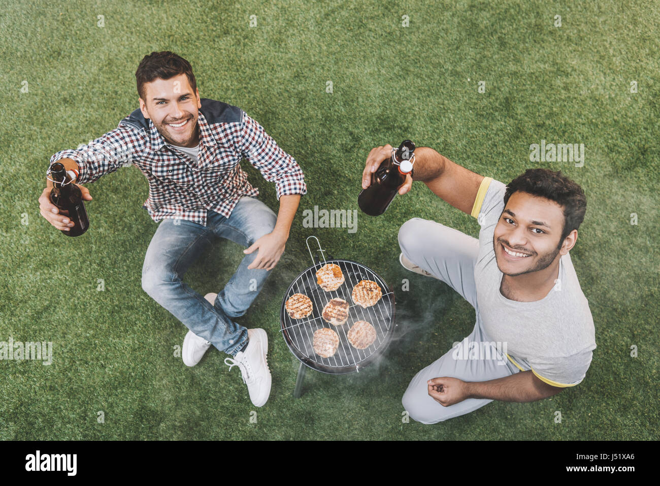 Portrait of happy young Men sitting on grass avec les bouteilles de bière et de faire un barbecue Banque D'Images