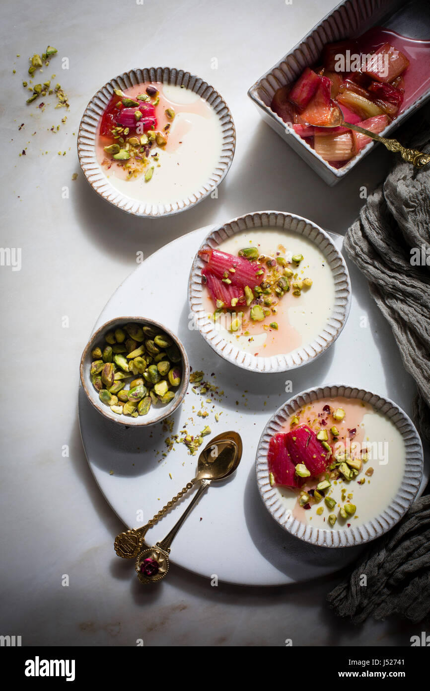 Pannacotta vanille classique garnie de pistaches hachées et de rhubarbe rôti dans une casserole au goût âpre en céramique sur une table en marbre sur une vue supérieure Banque D'Images