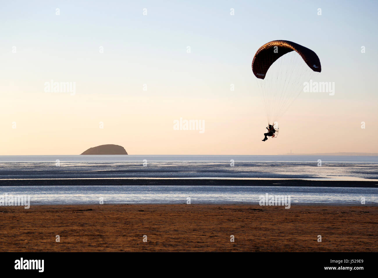 Une volée de parapente sur et le long de la ligne de rivage d'une plage déserte au coucher du soleil Banque D'Images