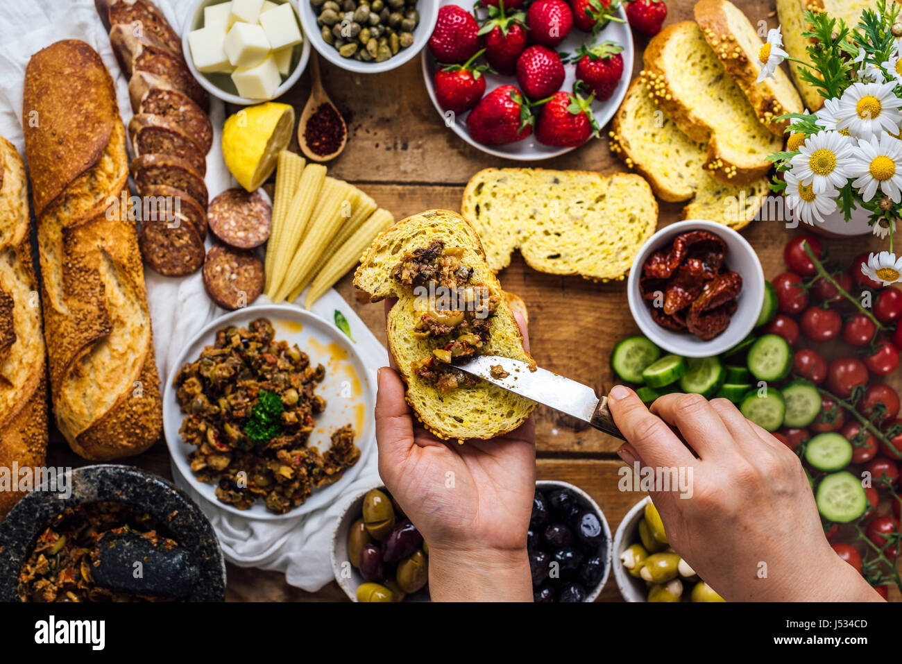 Une Femme La Diffusion De Tapenade D Olives Sur Une Tranche De Pain De Mais Baguette Francaise Saucisses Fromage Cors Bebe Strawberr Es Fleurs Tomates Et Concombre Photo Stock Alamy