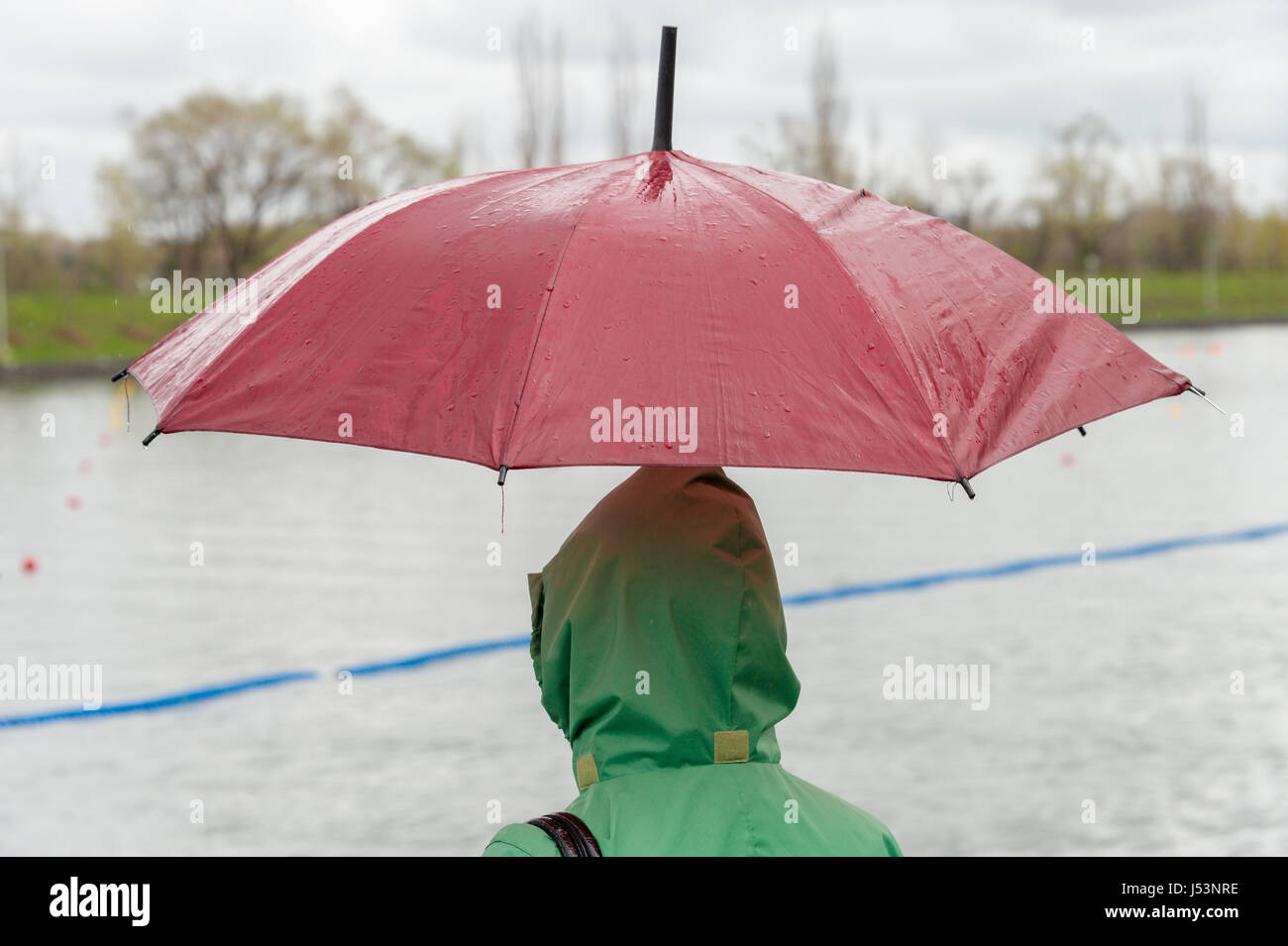 Quelqu'un vêtu d'un imperméable vert et tenant un parapluie rouge sur un jour de pluie Banque D'Images