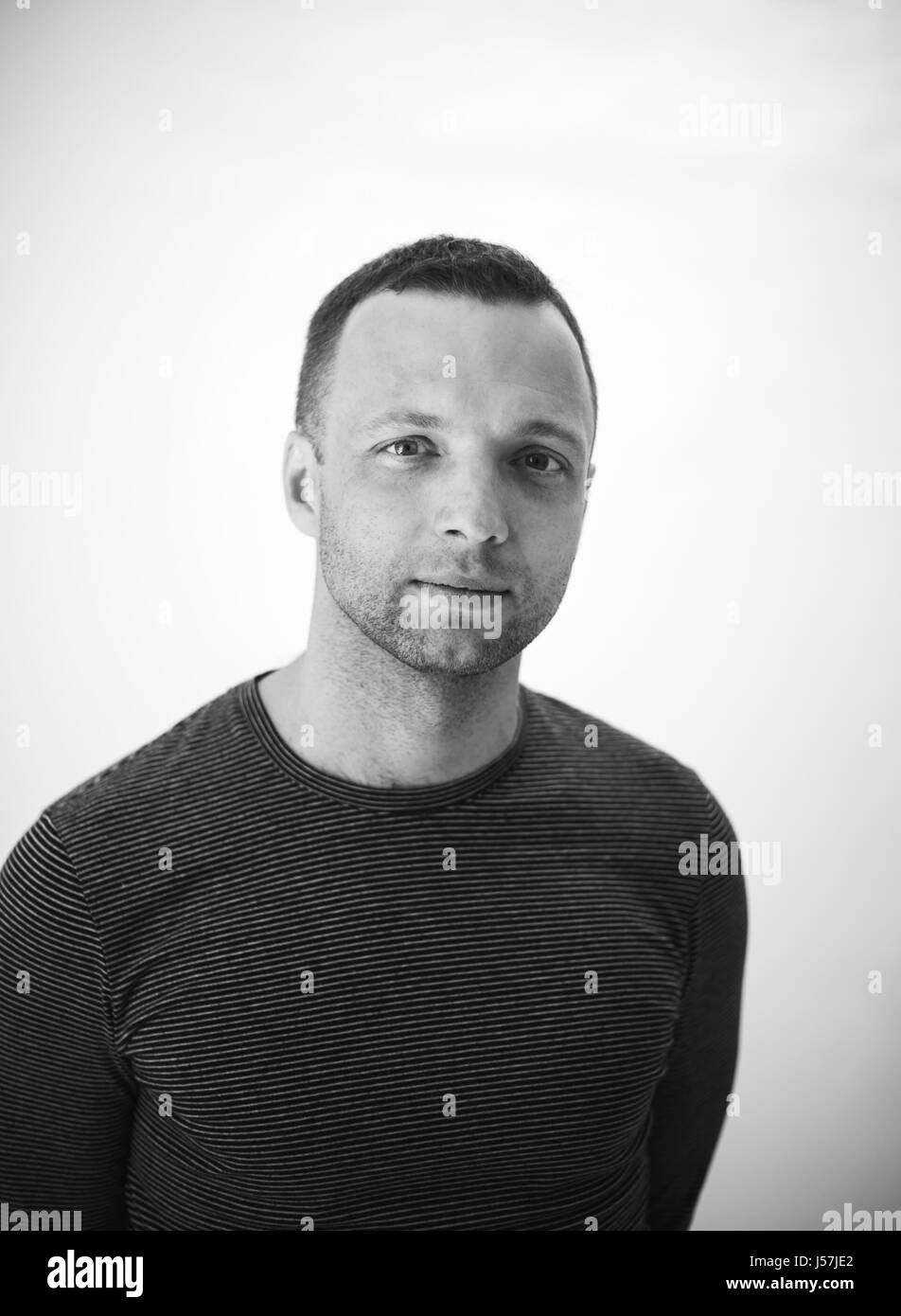 Studio portrait of young adult man standing européen sur mur blanc, noir et blanc photo verticale Banque D'Images